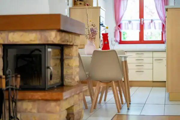 Blick in Richtung Küche, vorne links Kamin und dahinter Stühle, Tisch und Küchenzeile