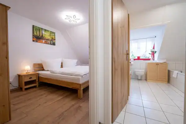 links Blick Schlafzimmer mit Doppelbett und Nachttisch, rechts Blick ins Bad mit Badewanne und WC