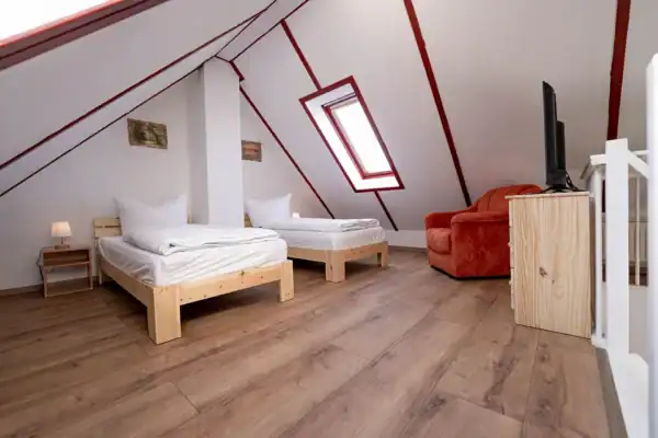 Dachgeschoss mit Schlafgalerie, vorne rechts offene Treppe nach unten daneben Kommode mit TV, hinten recht Sessel, hinten mitte 2 Einzelbetten mit Nachttisch