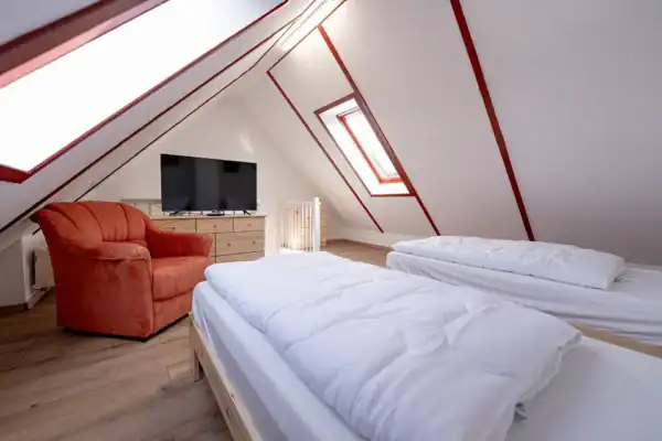 Dachgeschoss mit offener Schlafgalerie, vorne 2 Einzelbetten, hinten links Sessel und Kommode mit TV, hinten mitte offene Treppe nach unten