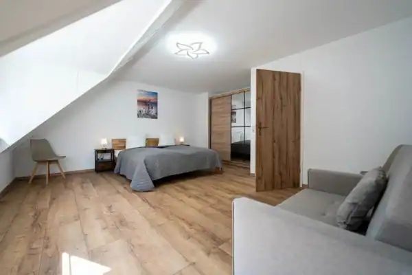 Schlafzimmer 1.OG, vorne rechts kleines Sofa und rechts daneben Eingangstür, hinten links Stuhl, hinten mitte Doppelbett, hinten rechts Kleiderschrank
